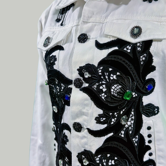 White denim jacket with black floral embroidery and colorful beads on a light gray background