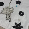 Close-up of a white denim jacket with black lace appliqué and colorful stones.