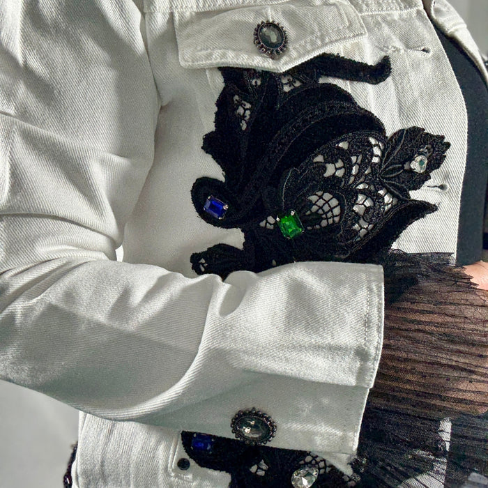 Close-up of a white denim jacket with black lace appliqué and colorful stones.